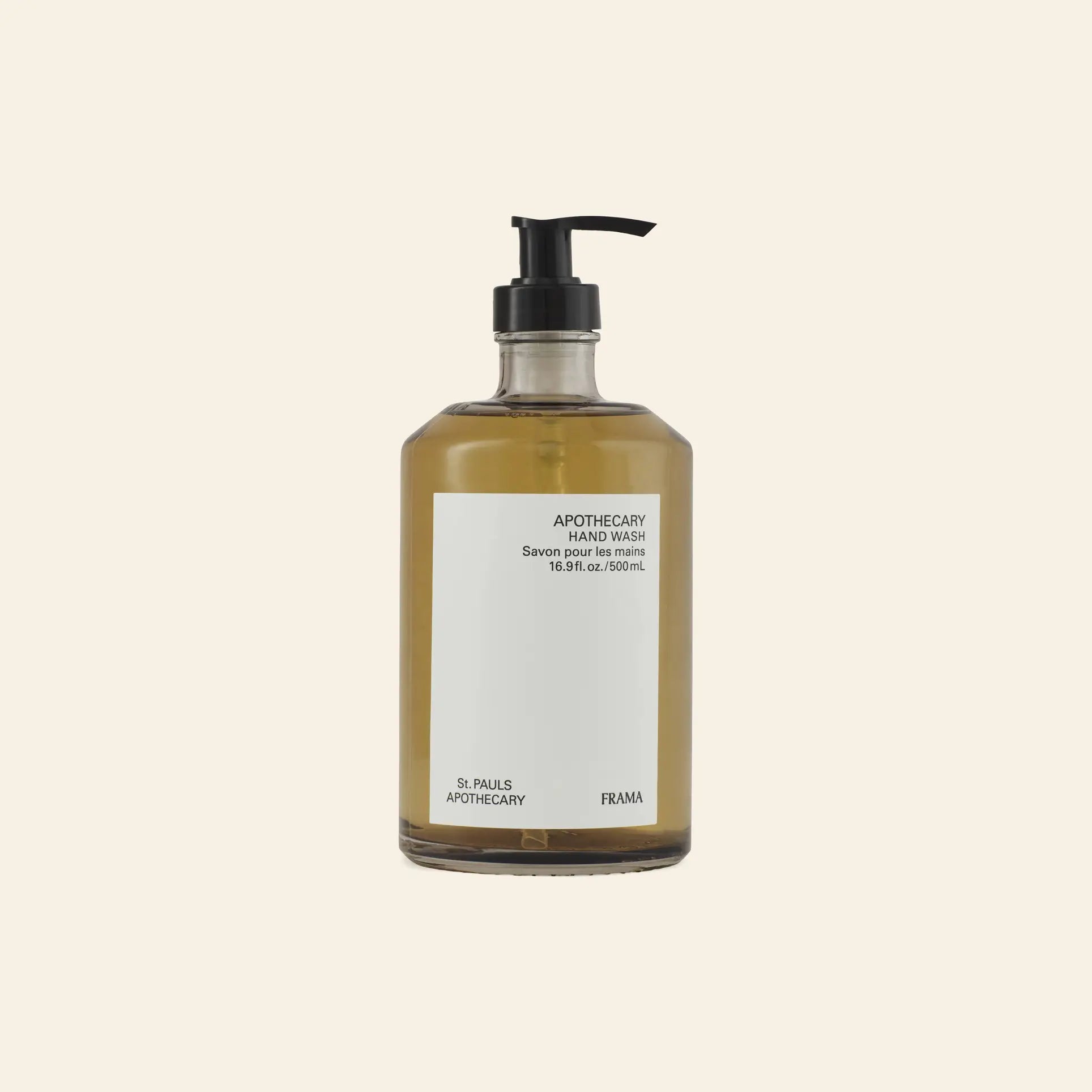 A clear pump bottle of FRAMA Hand Wash, 500ml, with amber liquid is shown with wooden collectibles against a beige background.