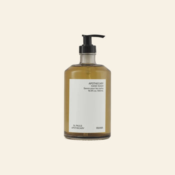A clear pump bottle of FRAMA Hand Wash, 500ml, with amber liquid is shown with wooden collectibles against a beige background.