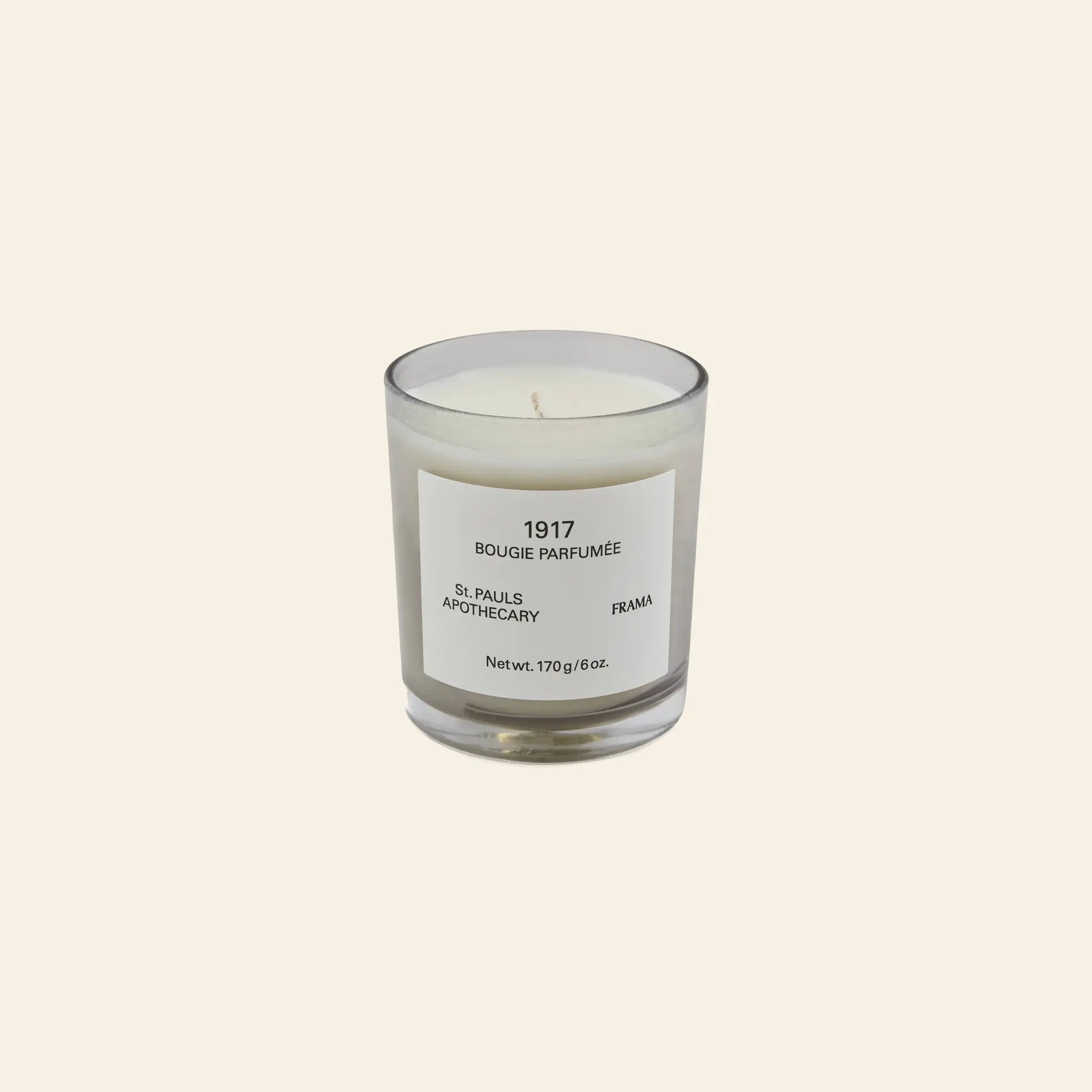 The FRAMA 1917 Scented Candle, 170g, in a clear glass holder with a minimalist label rests on a light beige background, capturing classical Chypre notes inspired by Mediterranean flora.