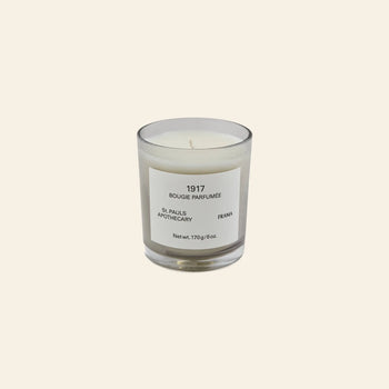 The FRAMA 1917 Scented Candle, 170g, in a clear glass holder with a minimalist label rests on a light beige background, capturing classical Chypre notes inspired by Mediterranean flora.