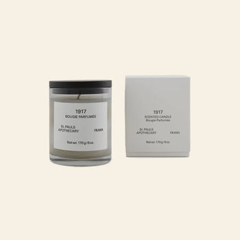 The FRAMA 1917 Scented Candle, 170g, with a black lid and white “1917 Bougie Parfumée” label, sits beside its box on a light beige background, reflecting FRAMAs nod to the timeless allure of classical Chypre.