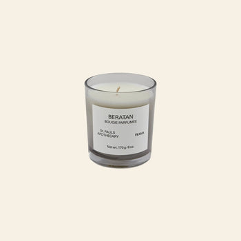 The FRAMA Beratan Scented Candle, 170g, in a clear glass jar with a BERATAN BOUGIE PARFUMÉE label adds warm fragrance and tropical ambiance, showcased on a light beige background.