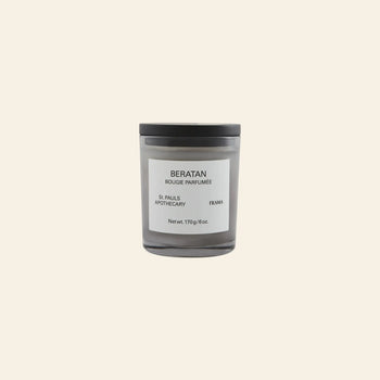 A gray FRAMA Beratan Scented Candle (170g) with a black lid and labeled BERATAN BOUGIE PARFUMÉE rests on a beige background, offering a warm fragrance with the signature Beratan scent.