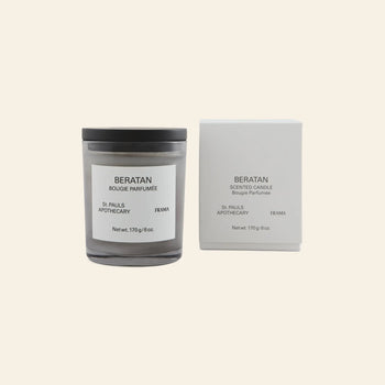 The FRAMA Beratan Scented Candle, 170g, in a glass jar with black lid sits beside its matching white box. Both are labeled FRAMA; its warm scent adds a tropical ambiance to any space.