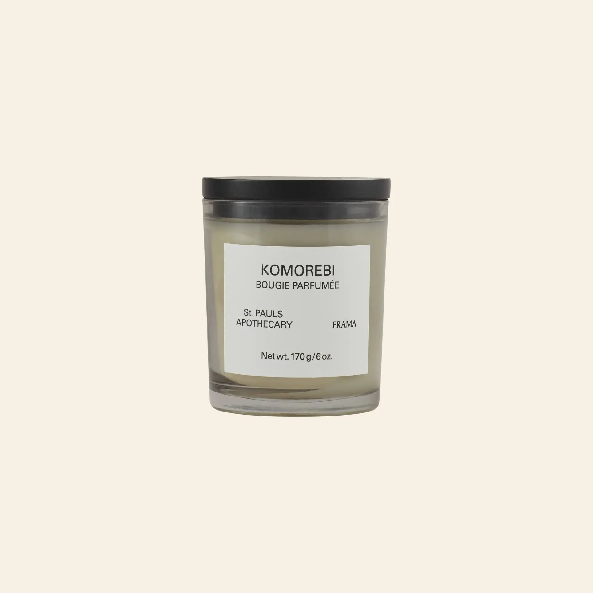 The FRAMA Komorebi Scented Candle, 170g, comes in a glass jar with a black lid and label, featuring an evocative aroma. Displayed against a plain beige background.