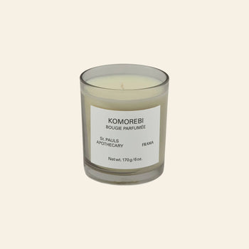 The FRAMA Komorebi Scented Candle, 170g, in a cream hue and clear glass jar with a white label, offers an evocative aroma against a light beige background.