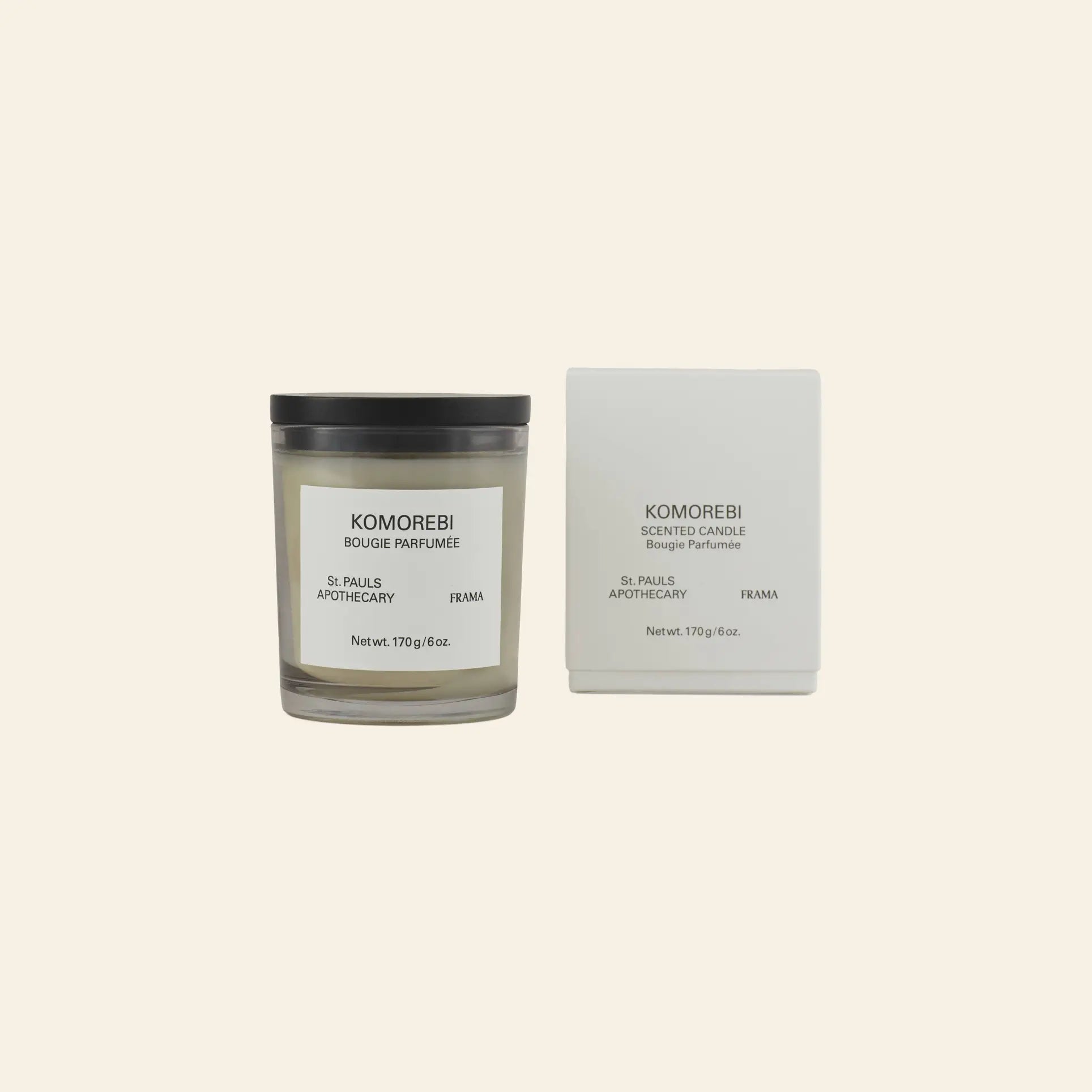 The FRAMA Komorebi Scented Candle, 170g, sits in a glass jar next to its matching white box on a light beige background. Both feature minimalist black branding, reflecting the refined elegance of this floral candle by FRAMA.