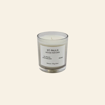 A FRAMA St. Pauls Scented Candle, 170g, sits in a clear glass jar with a minimalist label, displayed against a plain light beige background.