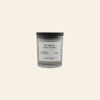 The FRAMA St. Pauls Scented Candle, 170g, in a glass jar with a black lid and minimalist white label, is displayed against a beige background.