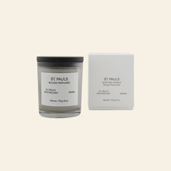The FRAMA St. Pauls Scented Candle, 170g, from the Apothecary Collection features a black lid and is shown next to its matching white box on a light beige background.