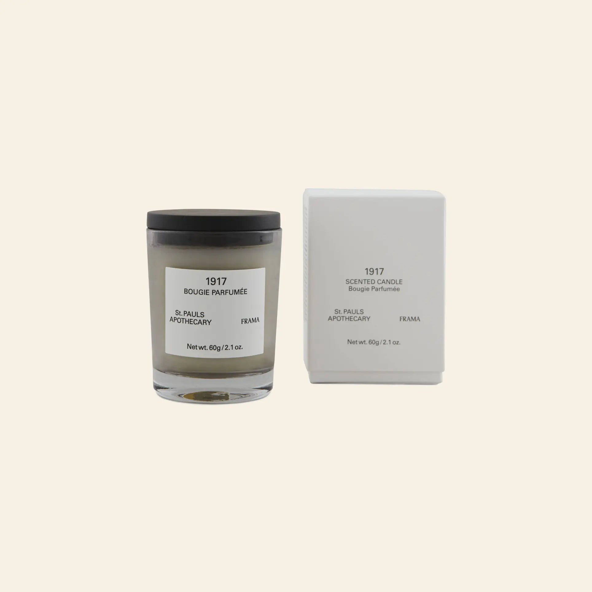 A FRAMA 1917 Scented Candle, 60g, in a glass jar is placed next to its matching white box on a light beige background. Both display the FRAMA brand and evoke Mediterranean flora.