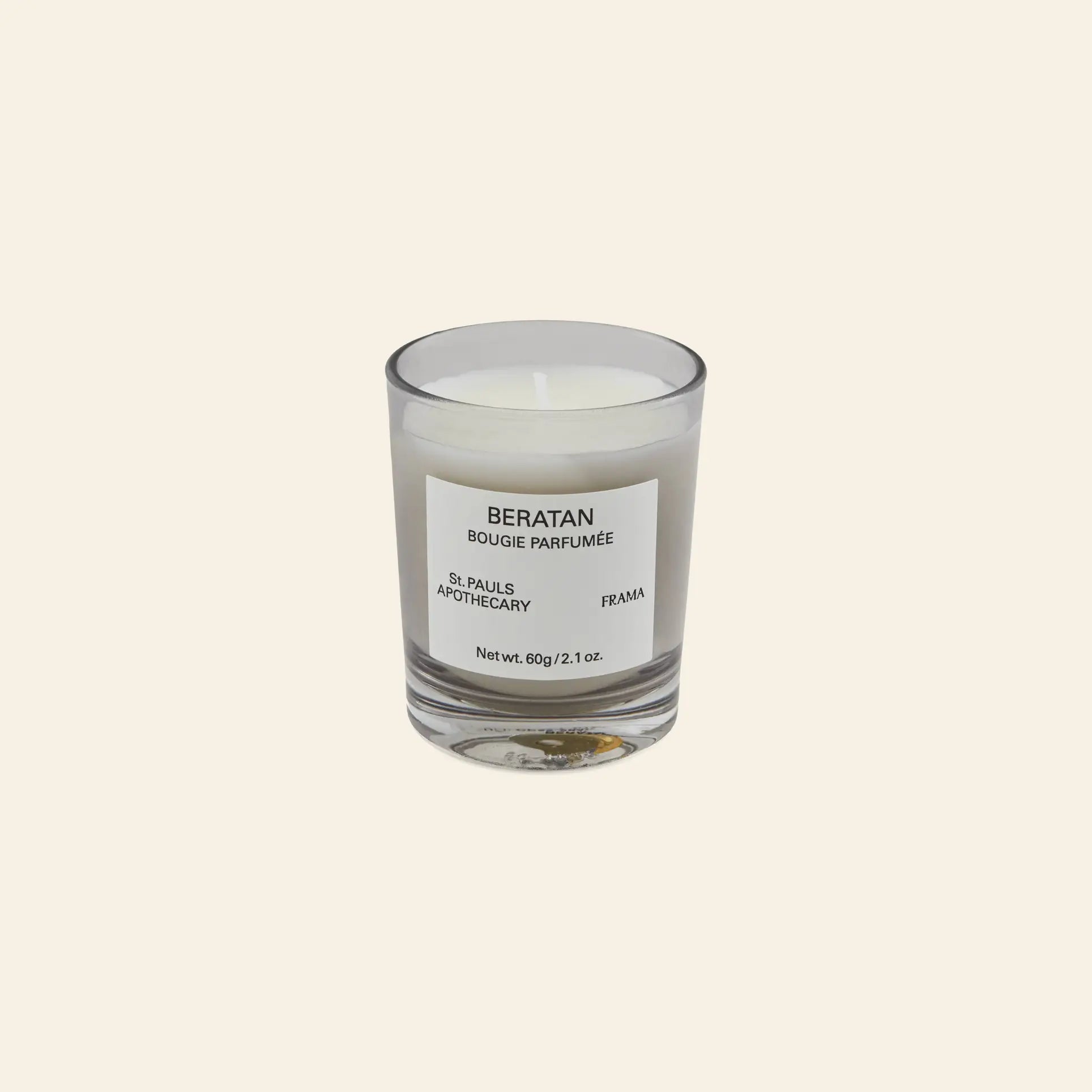 The FRAMA Beratan Scented Candle, 60g, features a clear glass holder with “BERATAN BOUGIE PARFUMÉE, ST. PAULS APOTHECARY, FRAMA” on the label, set against a beige background and offering a warm botanical fragrance.