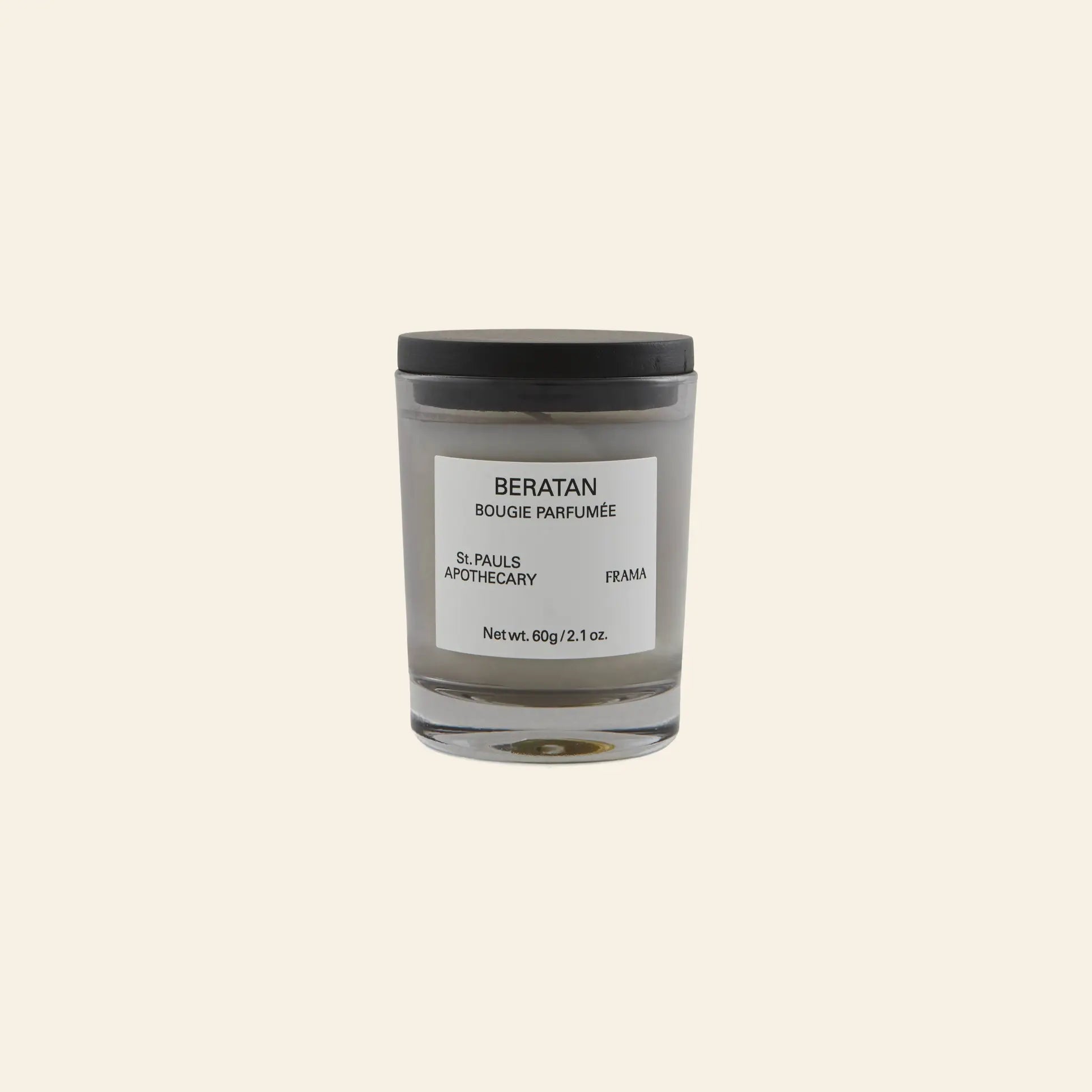 A minimalist white FRAMA Beratan Scented Candle, 60g, in a glass jar with black lid and label, offers a warm botanical fragrance. The candle is set against a plain beige background.