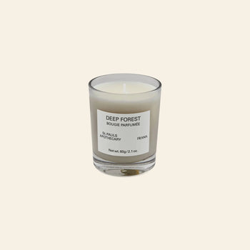 The FRAMA Deep Forest Scented Candle, 60g, in a clear glass holder with a Deep Forest Bougie Parfumée label, evokes the earthy scent of Abies fir woods and is displayed on a plain beige background.