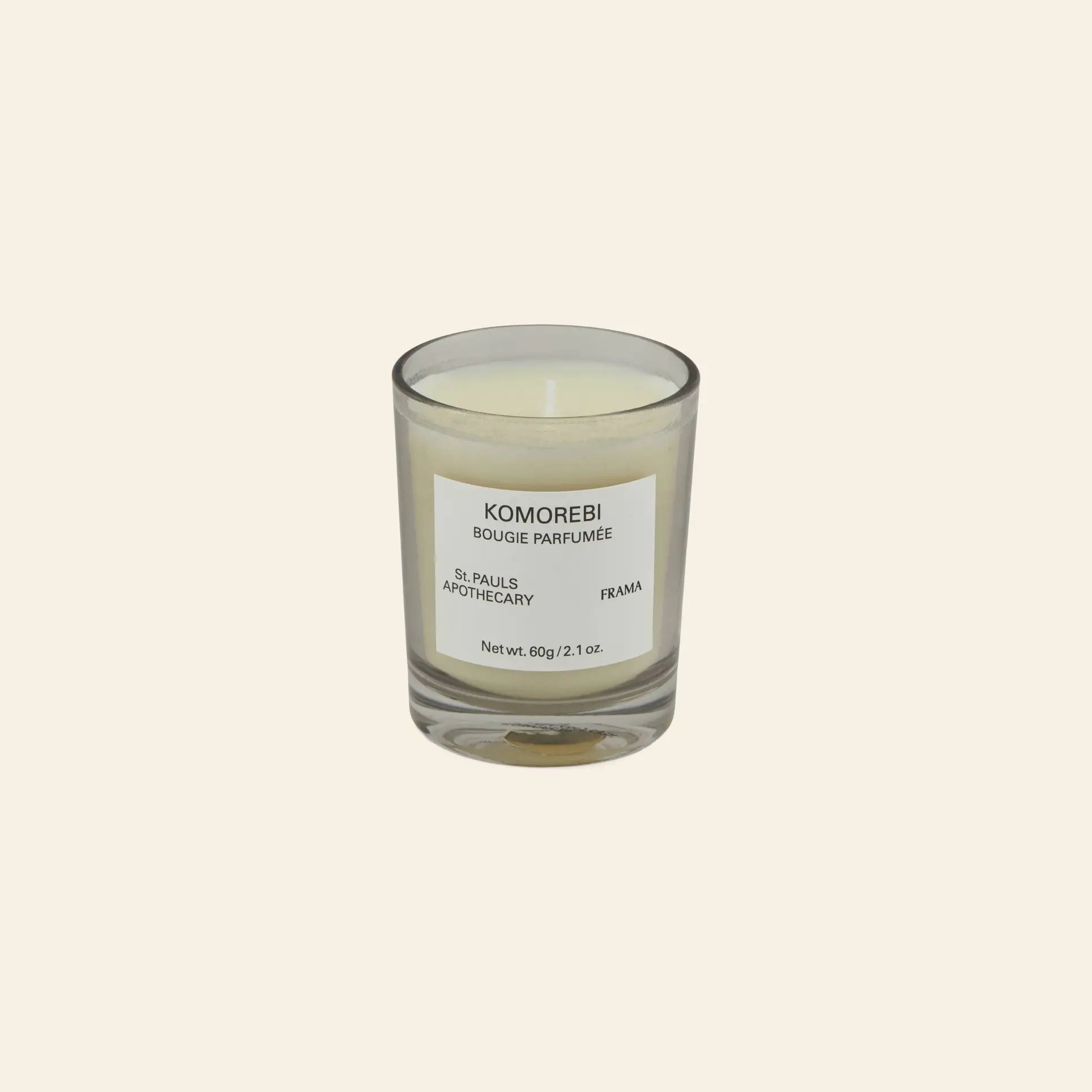 The FRAMA Komorebi Scented Candle, 60g, is a white candle in a clear glass holder with subtle floral notes, displayed against a plain beige background.