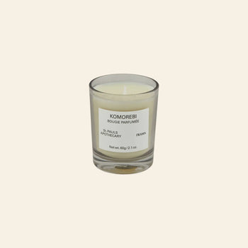 The FRAMA Komorebi Scented Candle, 60g, is a white candle in a clear glass holder with subtle floral notes, displayed against a plain beige background.