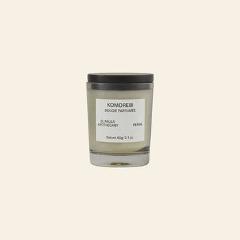 The FRAMA Komorebi Scented Candle, 60g, in a glass jar with a black lid and labeled with the brand name, sits on a beige background. This candle offers a delicate floral fragrance.