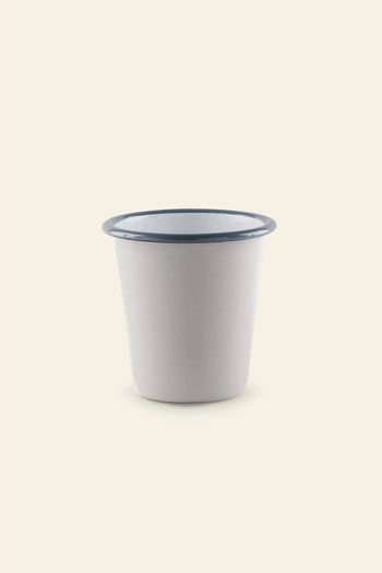 The Falcon Enamelware Tumbler by Falcon Enamelware, a plain white cup with a blue rim set against a light beige background, brings vintage style charm to any setting.