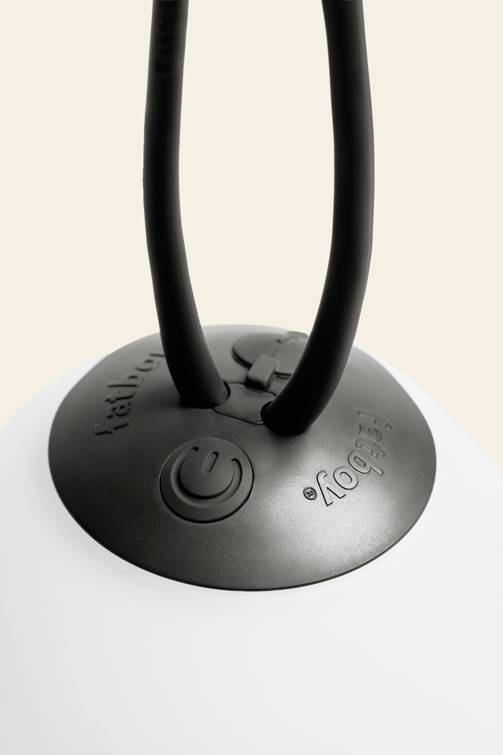 Close-up of the Fatboy Bolleke Mini La Surprise by Fatboy: a black circular base with embossed buttons and power symbol, two black cords extending upward, and adjustable dimming. The spherical lamp sits on a smooth white surface.