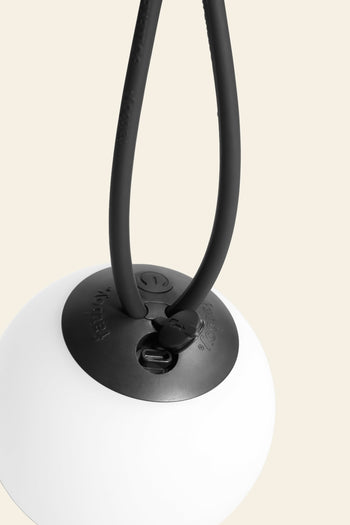 A close-up of the Fatboy Bolleke Mini La Surprise by Fatboy—a cordless spherical lamp with a black circular cap and two flexible cords—set against a light beige background.