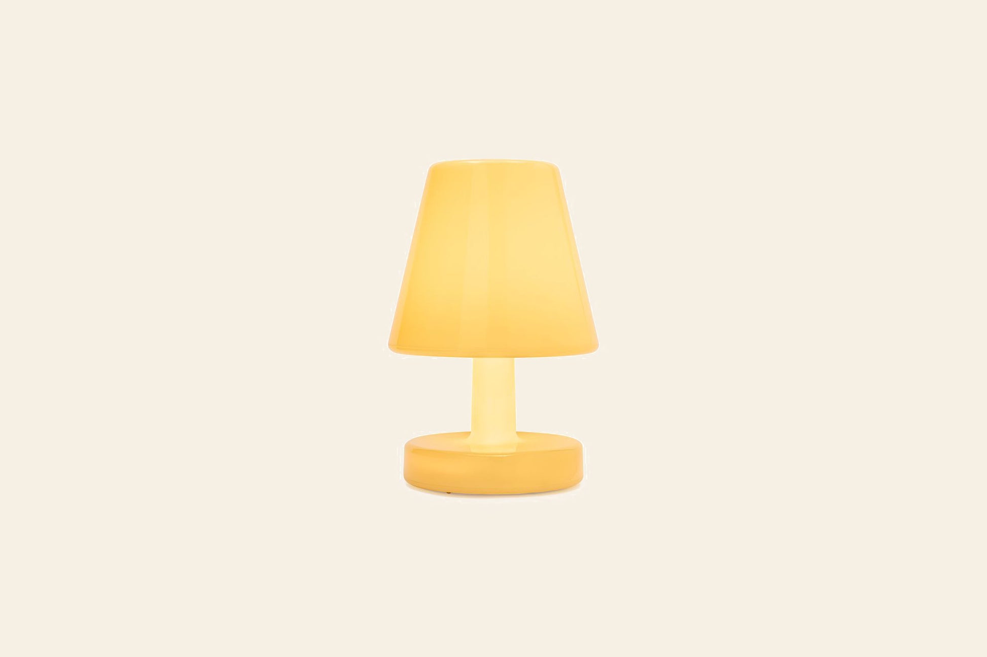 The Fatboy Edison The Ambiance by Fatboy is a modern yellow rechargeable table lamp with a conical shade and round base, illuminated and set against a plain light beige background.
