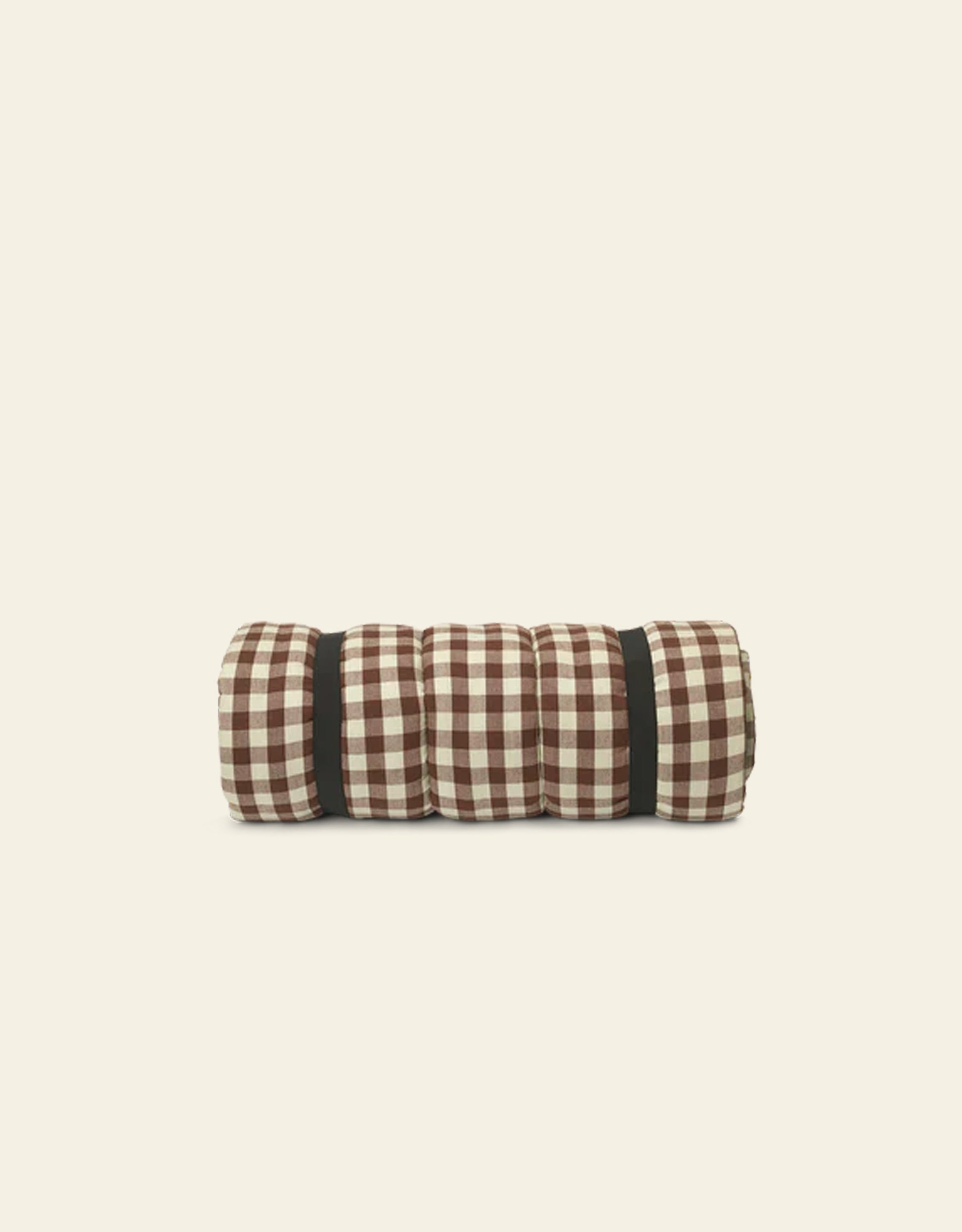 The Ferm Living Bothy Check Quilted Mattress features a brown and white checkered pattern, comes rolled up and secured with black straps, and is set on a light beige background—ideal for rustic home decor.