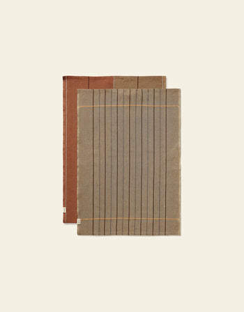 The Ferm Living Ito Tea Towel set includes two rectangular towels with a twill weave: one gray with black lines and beige borders, the other brown with subtle stripes—ideal kitchen textiles from Ferm Living.