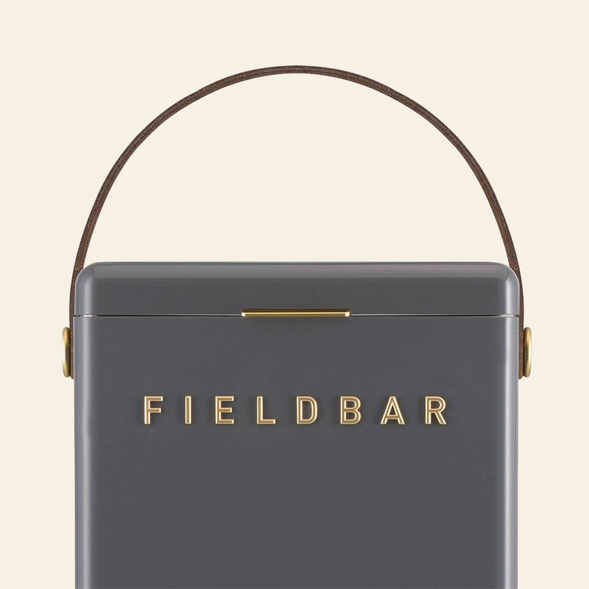 A close-up of the sleek, dark gray Fieldbar Drinks Box by Fieldbar features gold branding on the front, a slim brown side handle, and highlights its exceptional thermal performance.