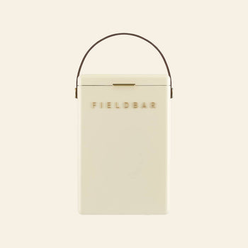 A cream-colored rectangular Fieldbar Drinks Box by FIELD BAR, featuring a brown handle and gold FIELD BAR lettering on the front, displayed against a plain light background.