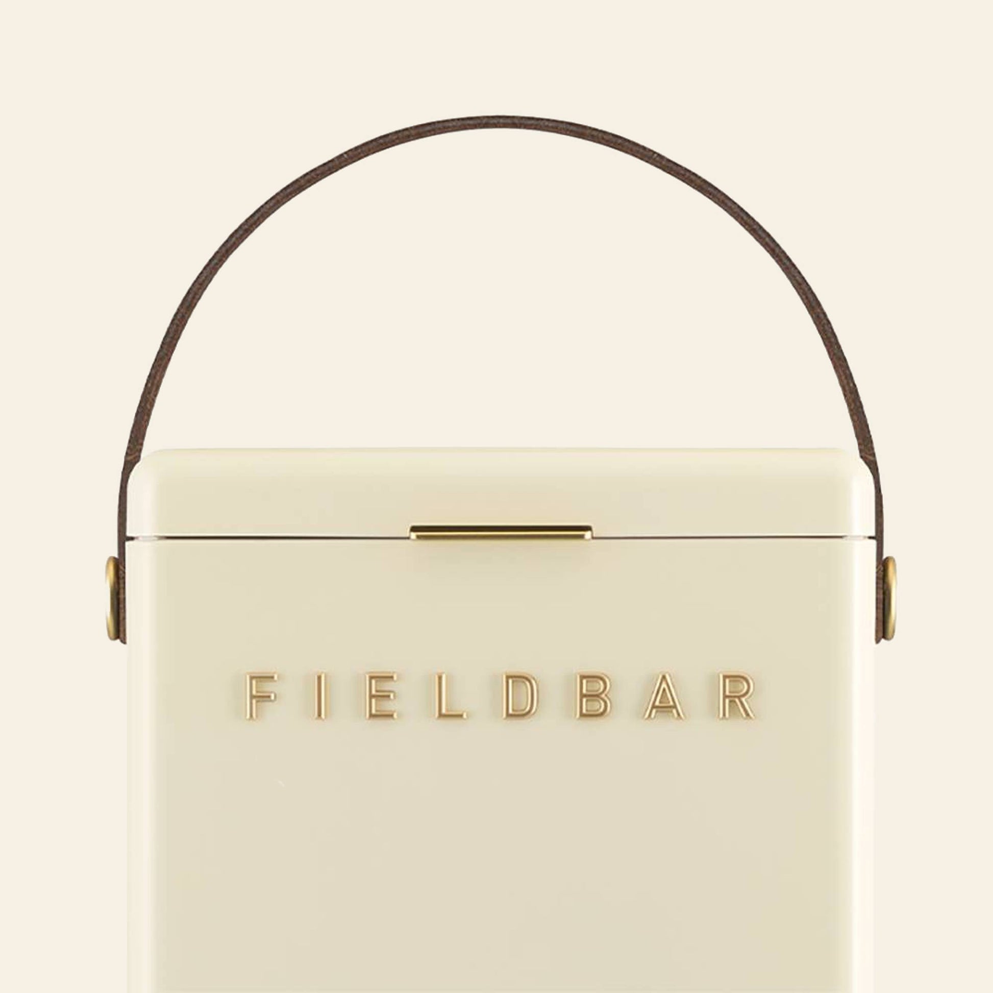 The cream-colored Fieldbar Drinks Box by Fieldbar features gold FIELD BAR lettering, a brown leather top handle, and outstanding thermal performance to keep drinks chilled.