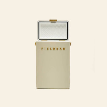 A cream-colored Fieldbar Drinks Box by Fieldbar stands upright with its lid open, showing a diamond-patterned white interior and gold FIELDBAR lettering on the front. The plain, light background highlights this ice box’s excellent thermal performance.