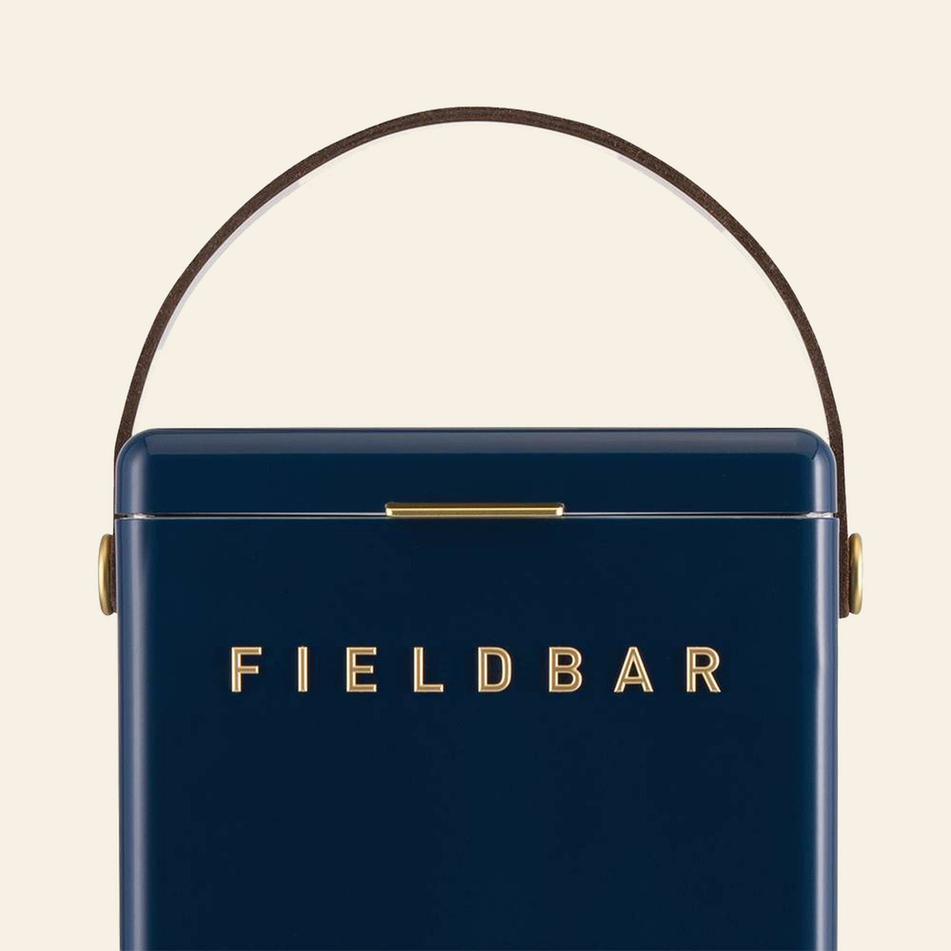 The Fieldbar Drinks Box is a navy blue rectangular cooler with a curved brown handle and gold hardware. FIELD BAR appears in gold on the front. This box provides excellent thermal performance against a light background.