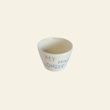 The Frizbee Ceramics Super Cup L by Frizbee Ceramics is a small white ceramic cup featuring blue handwritten text, MY MIND LONGER, on its side, photographed against a plain beige background.