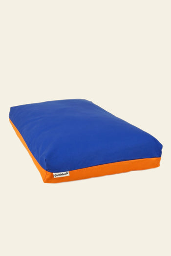 The Good Chonk Cloud Kapok Dog Bed is rectangular with a blue top, orange sides, and a small white good chonk label. It features eco-friendly kapok filling and a 100% cotton canvas cover, displayed on a plain light background.