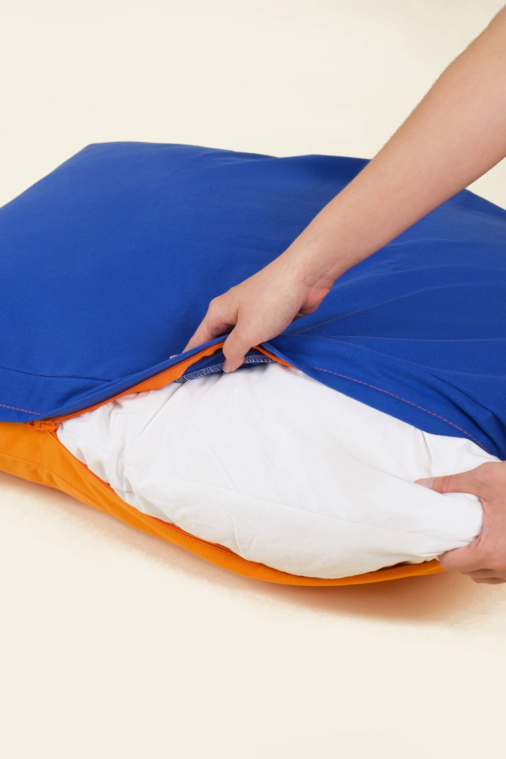 Someone unzips a blue and orange Good Chonk Cloud Kapok Dog Bed, revealing a white pillow inside with eco-friendly kapok fill and a 100% cotton canvas cover by Good Chonk.