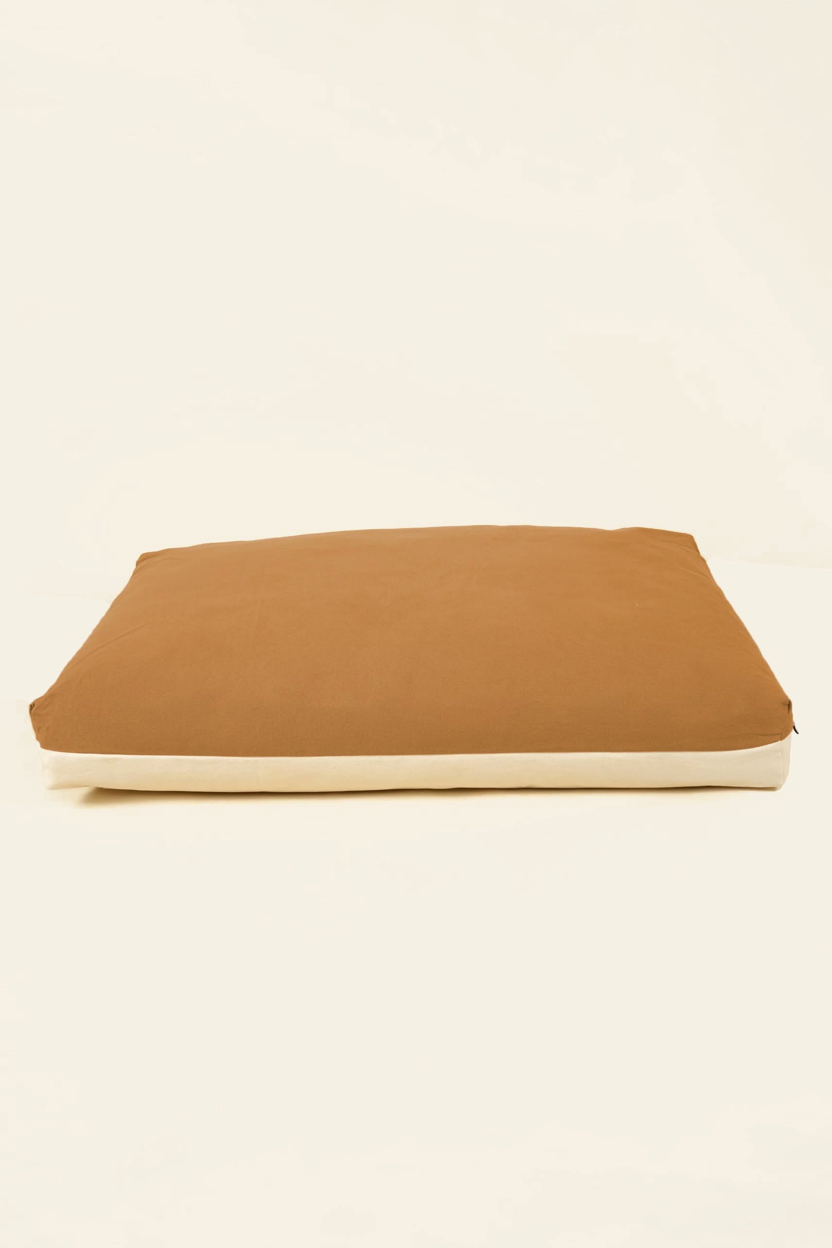 A rectangular brown Good Chonk Cloud Kapok Dog Bed with beige sides and a 100% cotton canvas cover rests flat on a light-colored surface.