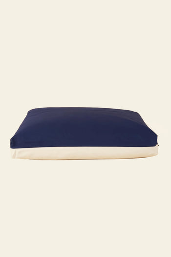 The Good Chonk Cloud Kapok Dog Bed features a rectangular shape, dark blue top, and white sides. Made by Good Chonk with a 100% cotton canvas cover and eco-friendly kapok fill, it’s pictured against a plain light background.