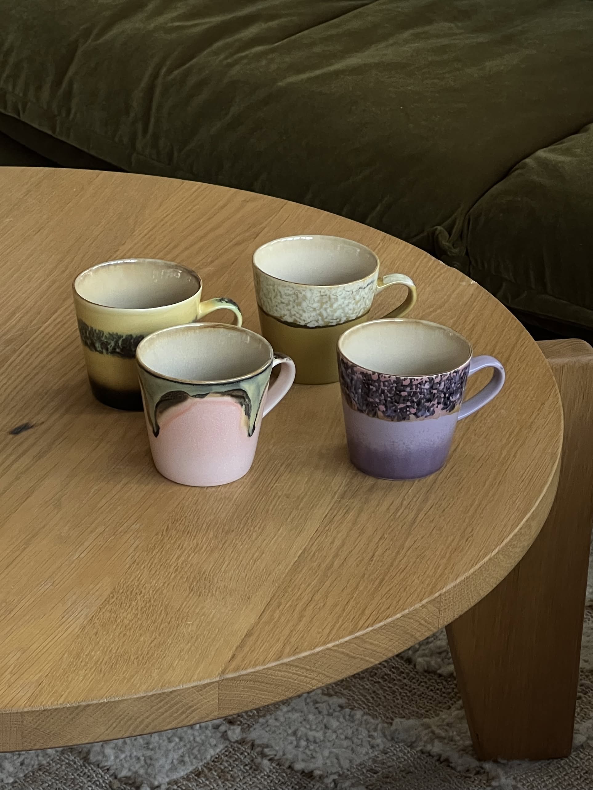 The HKLIVING 70s Ceramics: Americano Mugs, Set of 4 features hand-glazed stoneware in pastel shades and unique patterns, arranged on a round coffee table beside a green couch for retro charm.