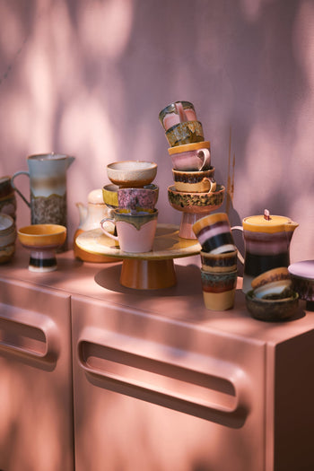 HKLIVING 70s Ceramics: Cappuccino Mugs, Set of 4 are arranged on and around a pink sideboard, with dappled sunlight and leafy shadows cast across a pink wall in the background.