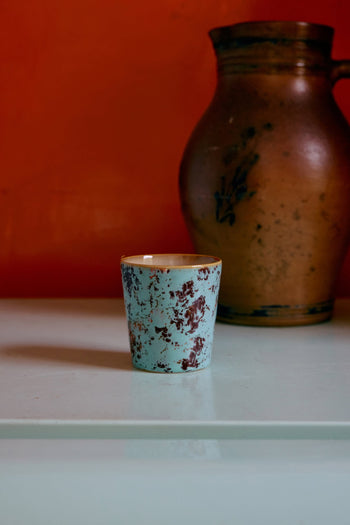 An HKLIVING 70s Ceramics Coffee Mug from the set of 6 is displayed on a pale surface in front of a large brown jug, with an orange wall as the backdrop.
