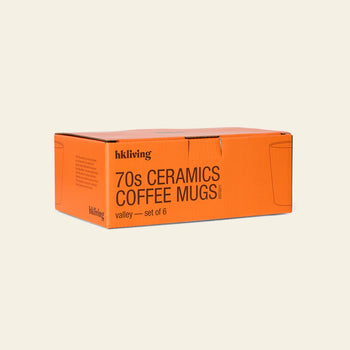 An orange box labeled HKLIVING 70s Ceramics: Coffee Mugs, Set of 6 is displayed against a plain light background, featuring simple mug line drawings and evoking the handcrafted glazing style of 70s ceramics.