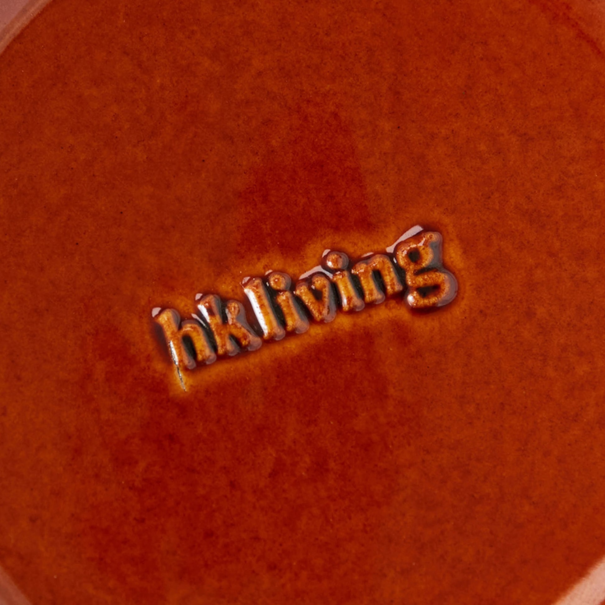 A close-up of a textured, reddish-brown ceramic dessert bowl from the HKLIVING 70s Ceramics: Dessert Bowls, Set of 4 shows the glazed, embossed HKLIVING logo at the center, highlighting its retro-inspired design.
