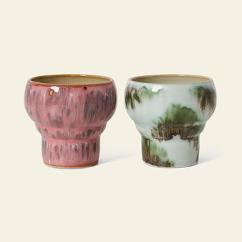 The HKLIVING 70s Ceramics: Lungo Mugs, Set of 2 features retro stoneware mugs—one with pink textured vertical patterns and the other with a white and green marbled look. Both glossy mugs from HKLIVING sit on a light background.