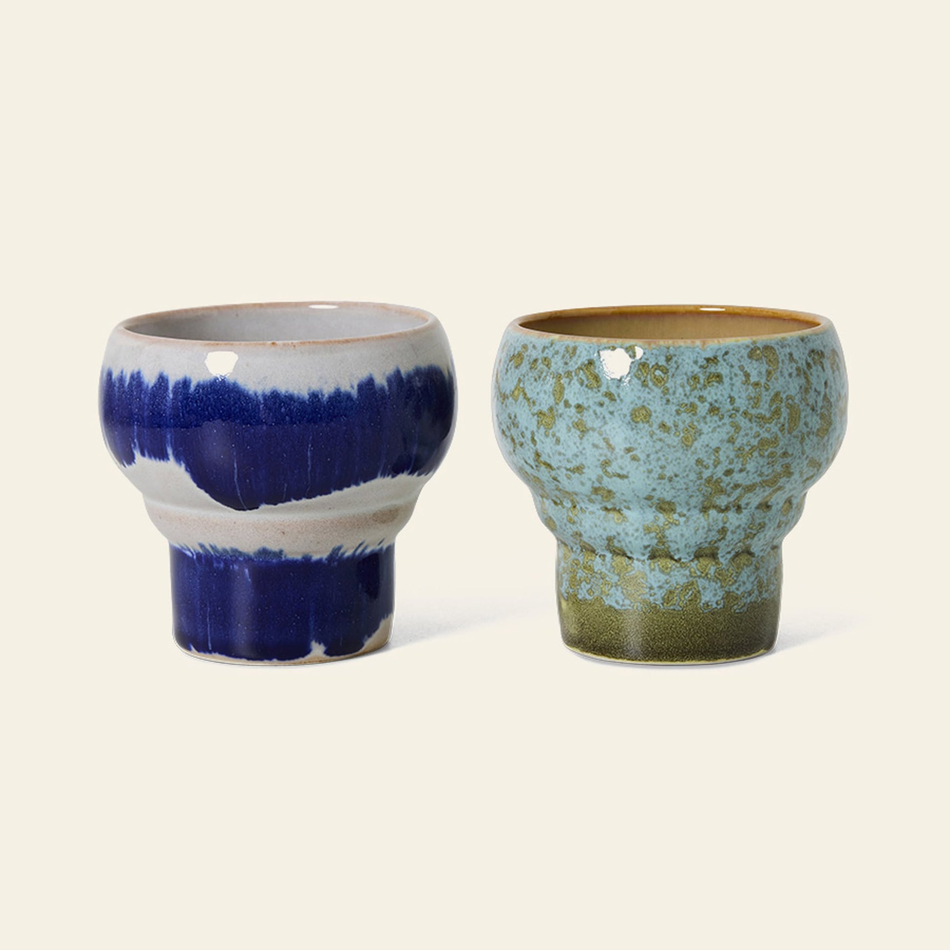 The HKLIVING 70s Ceramics: Lungo Mugs, Set of 2, features one blue and white glazed mug and one with a greenish speckled glaze accented by brown at the rim and base, both reflecting retro style on a light background.