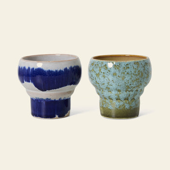 The HKLIVING 70s Ceramics: Lungo Mugs, Set of 2, features one blue and white glazed mug and one with a greenish speckled glaze accented by brown at the rim and base, both reflecting retro style on a light background.