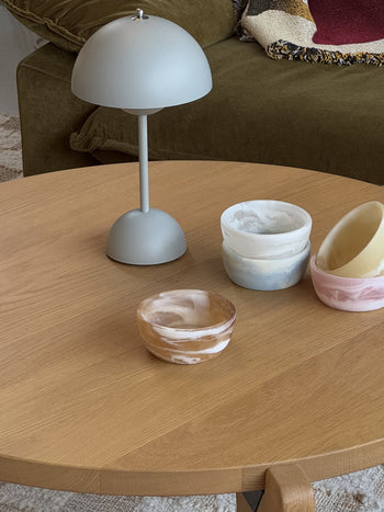 A round wooden coffee table displays four colorful HKLIVING Patio Bowls and a gray lamp, set in a cozy living room with a green sofa. These stylish HKLIVING bowls are perfect for effortless indoor or outdoor entertaining.