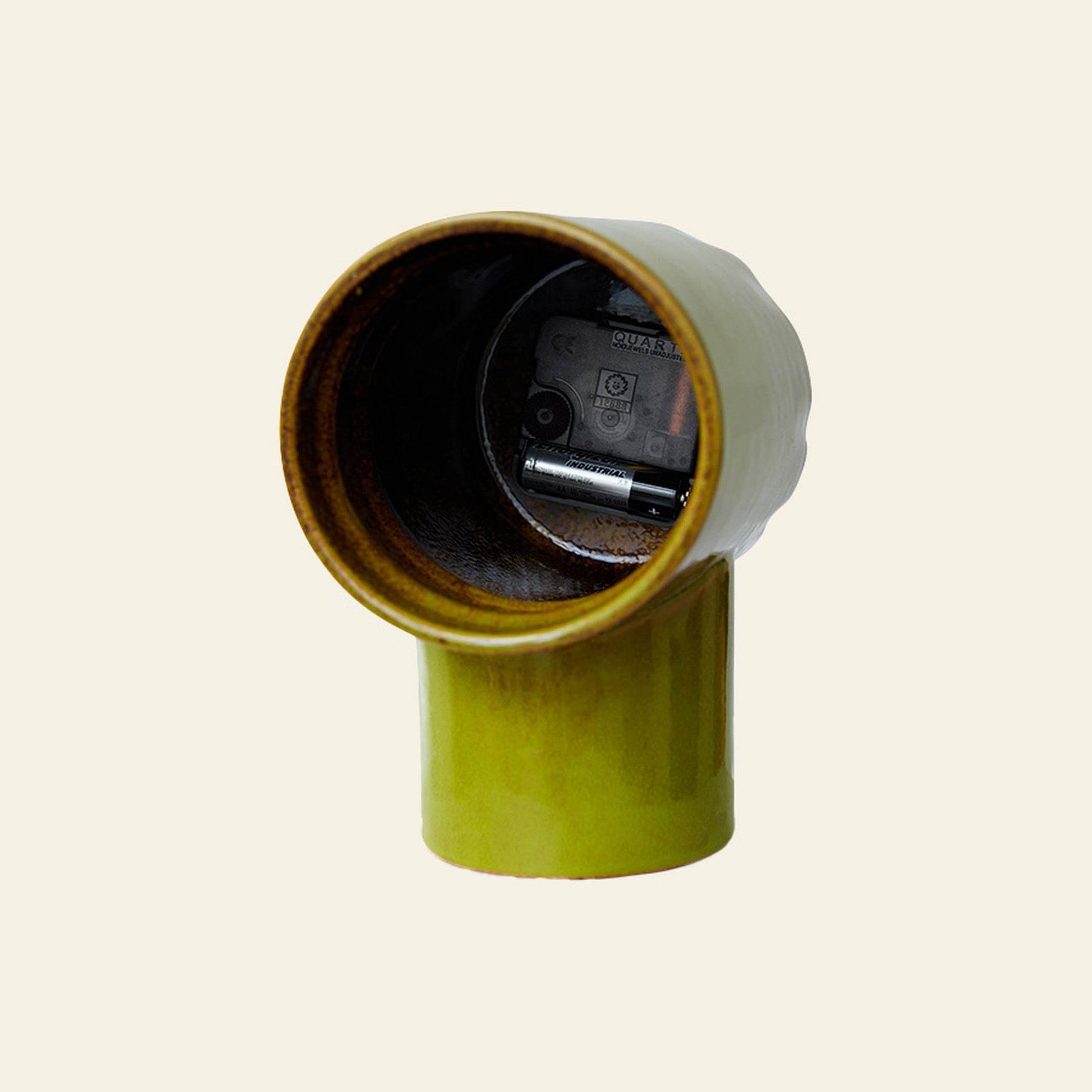 The HKLIVING Retro Ceramic Clock - Olive features a green ceramic body with a cylindrical base and open top, displaying its clock mechanism and battery. This nostalgic HKLIVING piece stands out against a plain, light background.