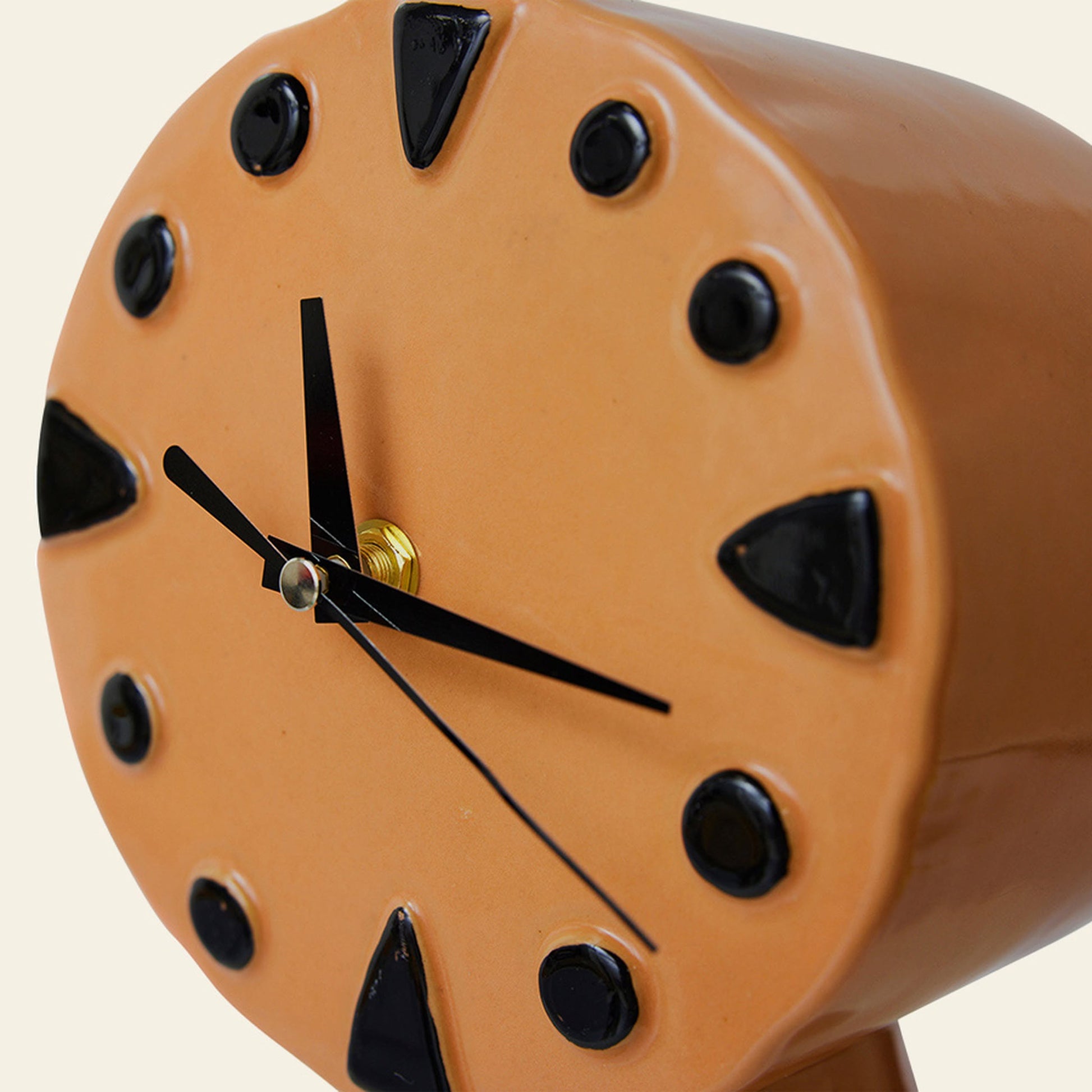 A close-up of the HKLIVING Retro Ceramic Clock - Peach shows its round orange face, black geometric hour markers, and three black hands. This HKLIVING clock features a vintage-inspired look crafted with traditional firing techniques.