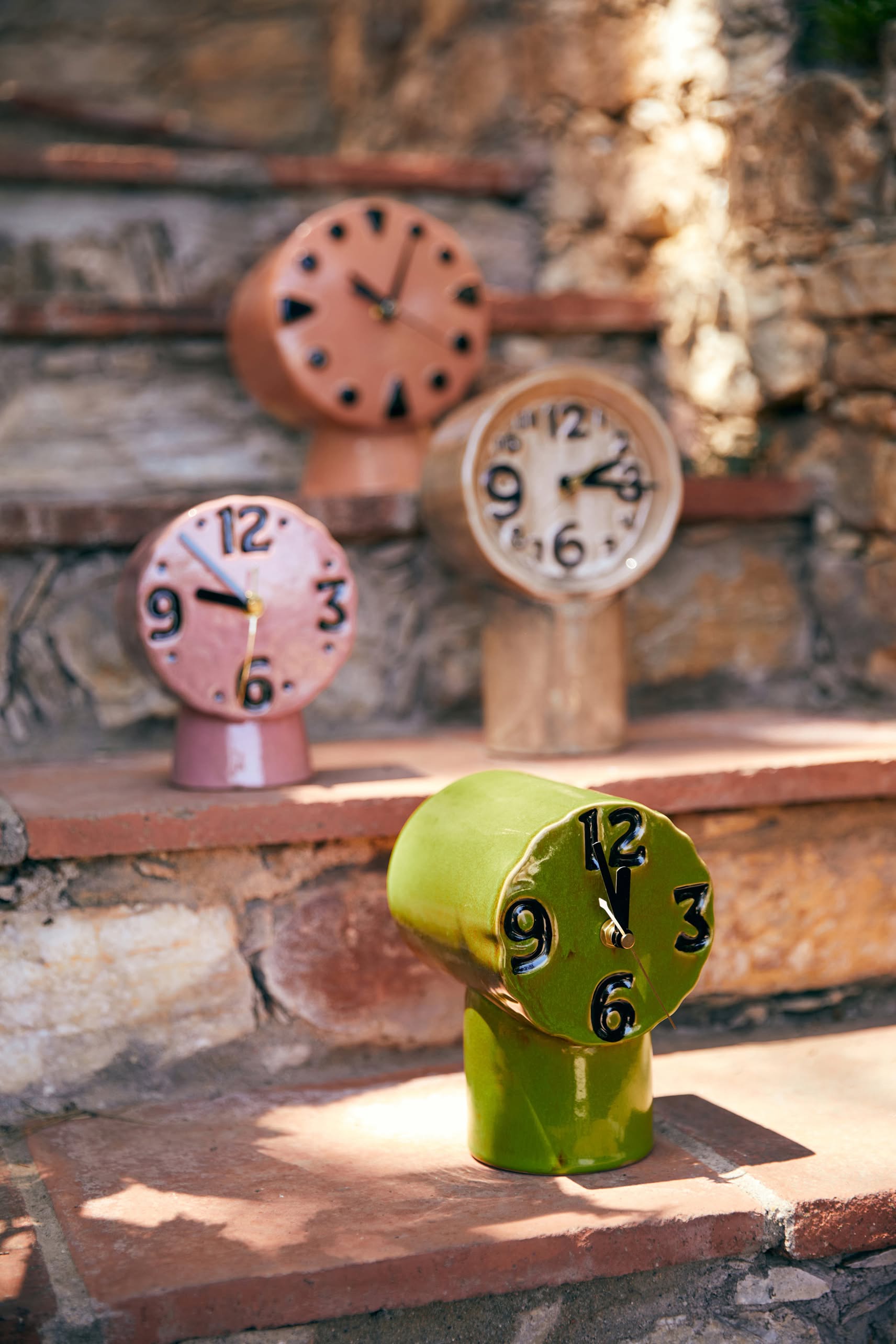The HKLIVING Retro Ceramic Clock – Peach, by HKLIVING, features a vintage-inspired design with distorted shapes and numbers in soft hues. Displayed on outdoor stone steps, its ceramic body glows in the sunlight for a stylish retro look.