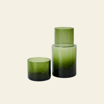 The HKLIVING Tube Carafe & Glass Set in Olive features cylindrical glassware with a dark-to-light green gradient, arranged elegantly against a beige background to bring contemporary style to your dining setting.